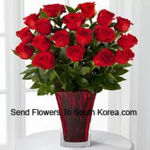 18 roses rouges avec des garnitures saisonnières dans un vase en verre décoré d'un nœud rose